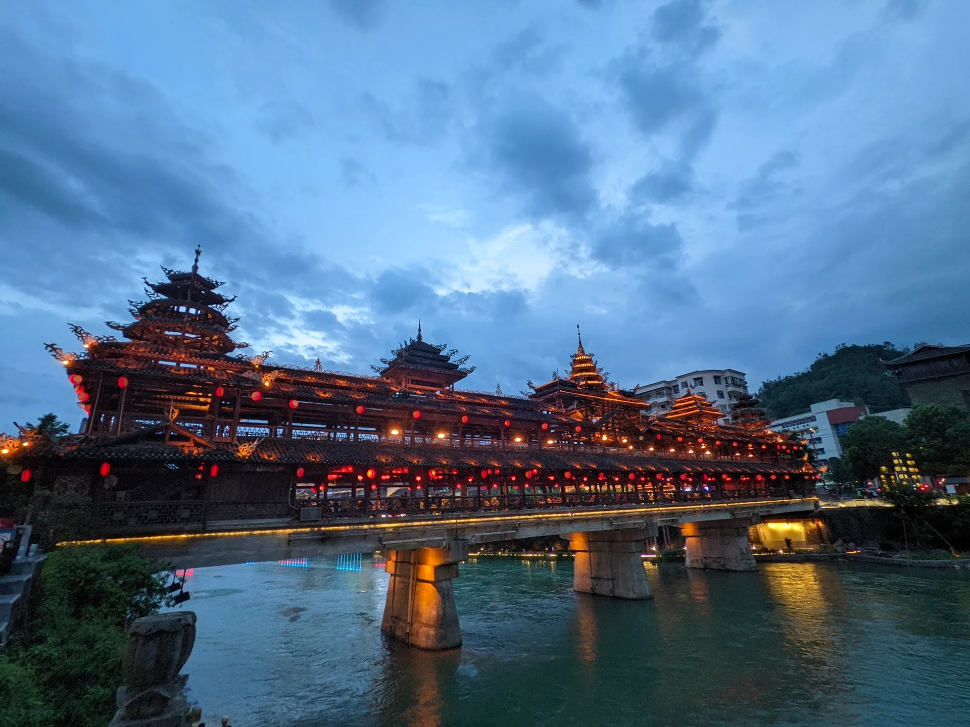 河畔楼阁在雨后亮起，灯火映入缓慢流动的水面。