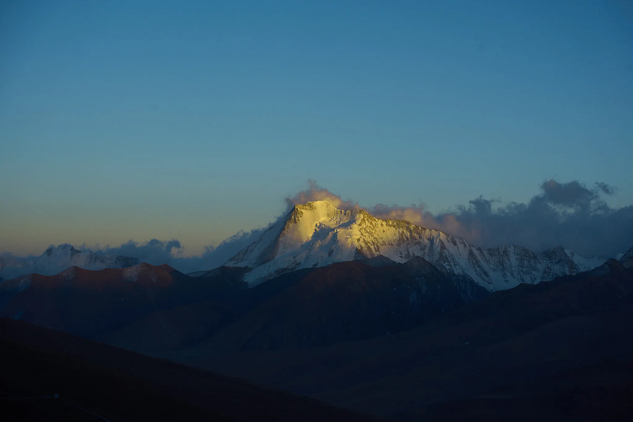晨昏金光只落在雪峰顶部，山脚仍沉在深蓝色阴影里。
